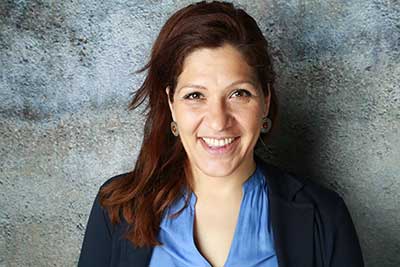 Frau Manjic lächelnd, stehend, vor Mauerhintergrund